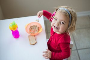 Little girl eating oatmeal and smiling up at the camera