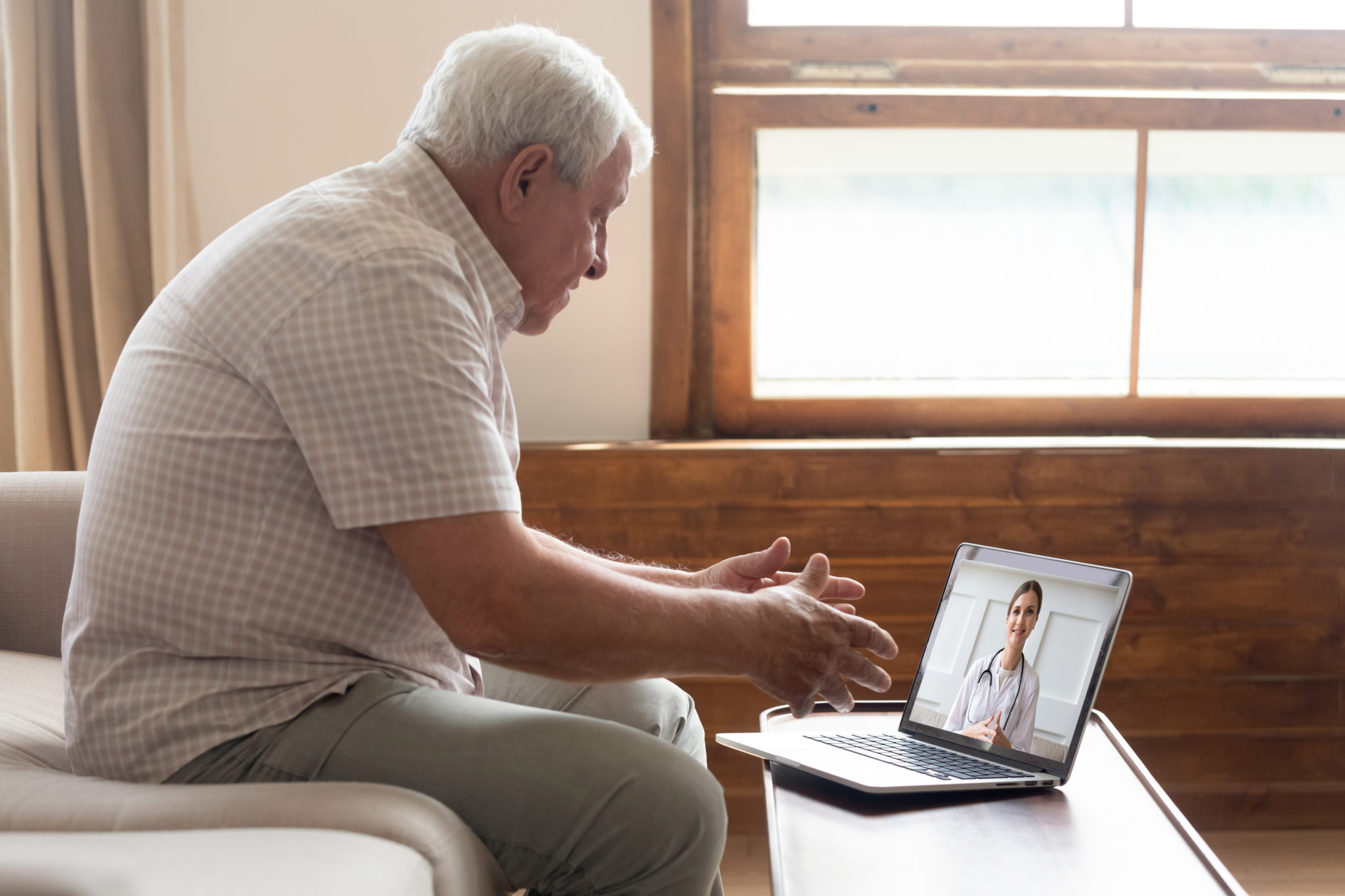 Elderly 70s man seated on sofa make distant video call with doctor