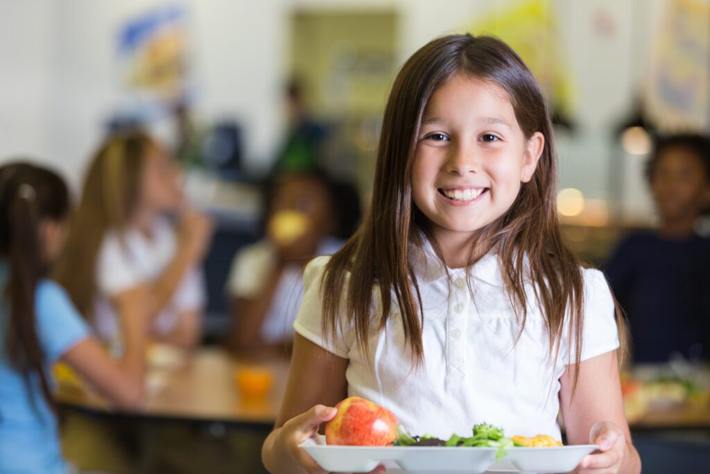 An elementary school student holding tray of food with fruits and veggies