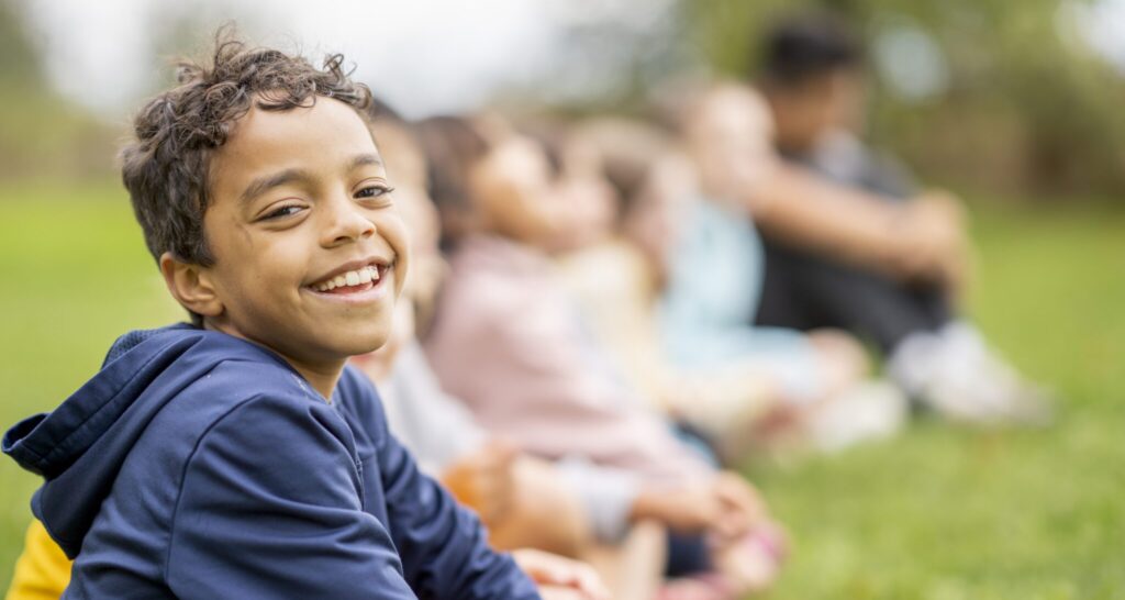 A boy smiles as he sits with his friends in a field