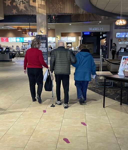 Community members attending the dementia friendly movie program are assisted through the theater lobby and guided by purple footprint makers showing the direction to the theater.